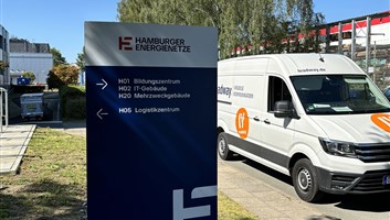 Monolith mit Wegweisern zu Bildungszentrum, IT-Gebäude und Logistikzentrum vor einem Firmengelände, daneben ein Montagefahrzeug von Leadway