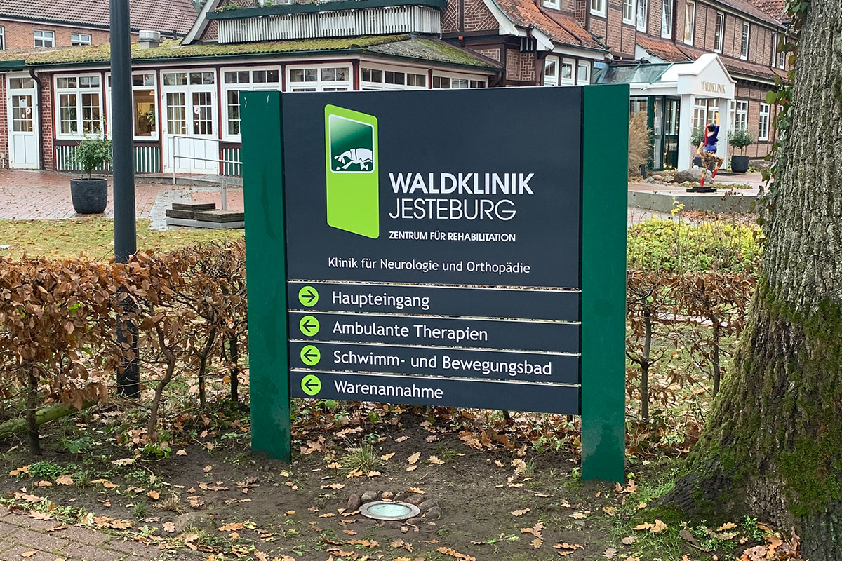 Zweipfostige Beschilderungsanlage der Waldklinik Jesteburg mit vier Wegweiserleisten zu Haupteingang, ambulanten Therapien, Schwimm- und Bewegungsbad und Warenannahme