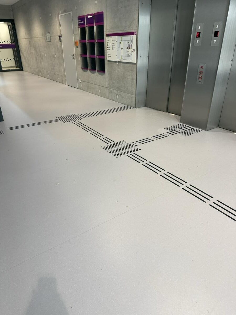 Etagenübersicht des Erdgeschosses und Wegweiser an den Aufzügen im CAU-Design, davor das taktile Bodenleitsystem