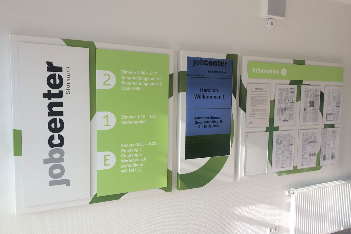 Hausübersicht des Jobcenters Stormarn mit Etagenverzeichnis, digitaler Willkommenstafel und Informationsvitrine an einer Wand