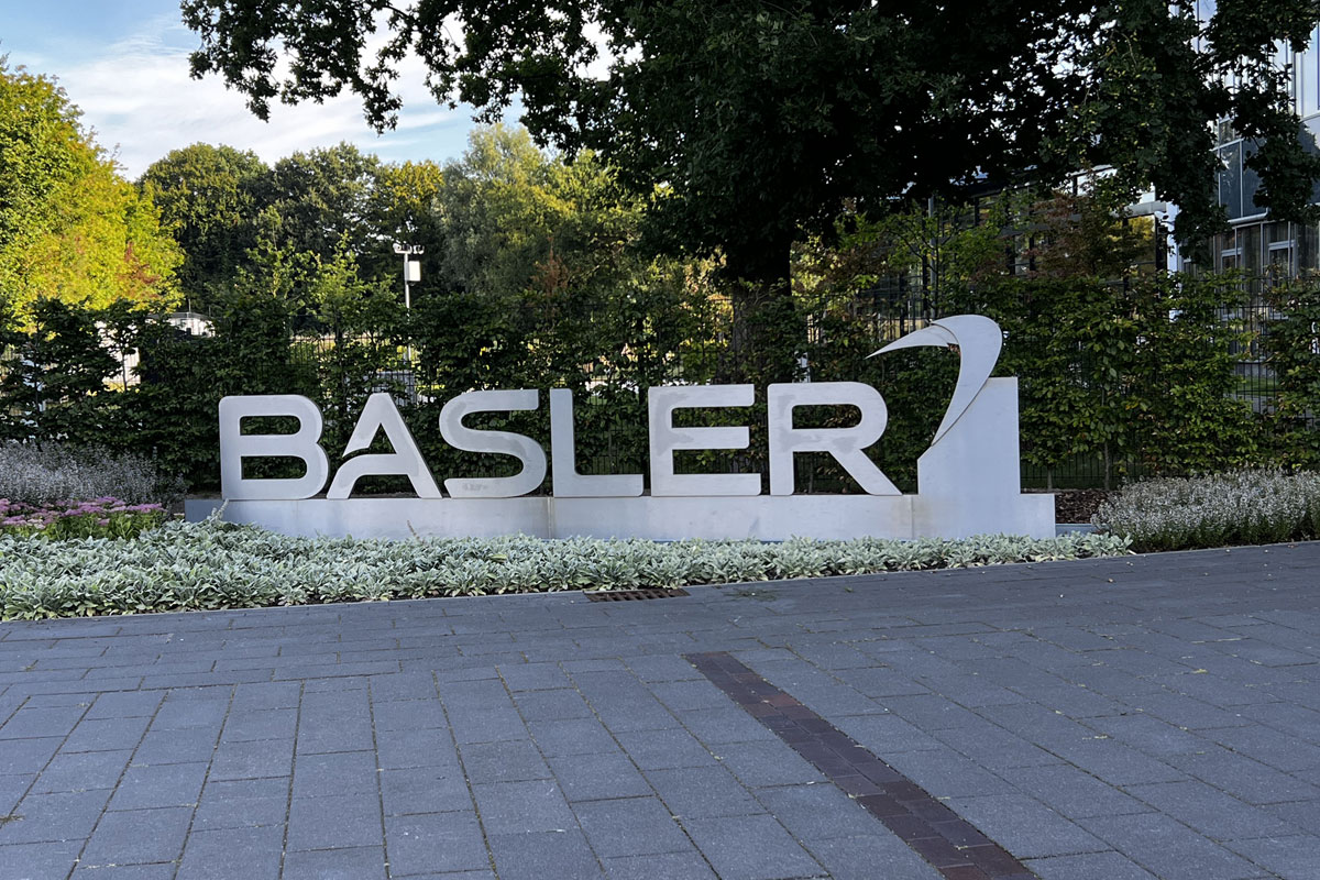 Freistehende weiße Einzelbuchstaben des Schriftzugs BASLER mit Logo auf einem Sockel in einem Staudenbeet