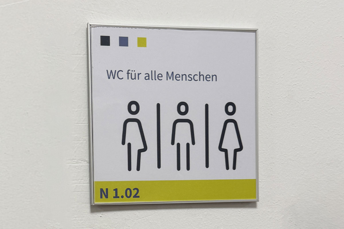 Türschild im Wechselrahmen mit der Aufschrift WC für alle Menschen, drei Personenpiktogrammen und der Raumnummer N 1.02