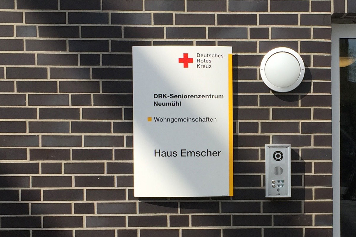 Wandschild mit DRK-Logo an einer Klinkerfassade: DRK-Seniorenzentrum Neumühl, Wohngemeinschaften, Haus Emscher