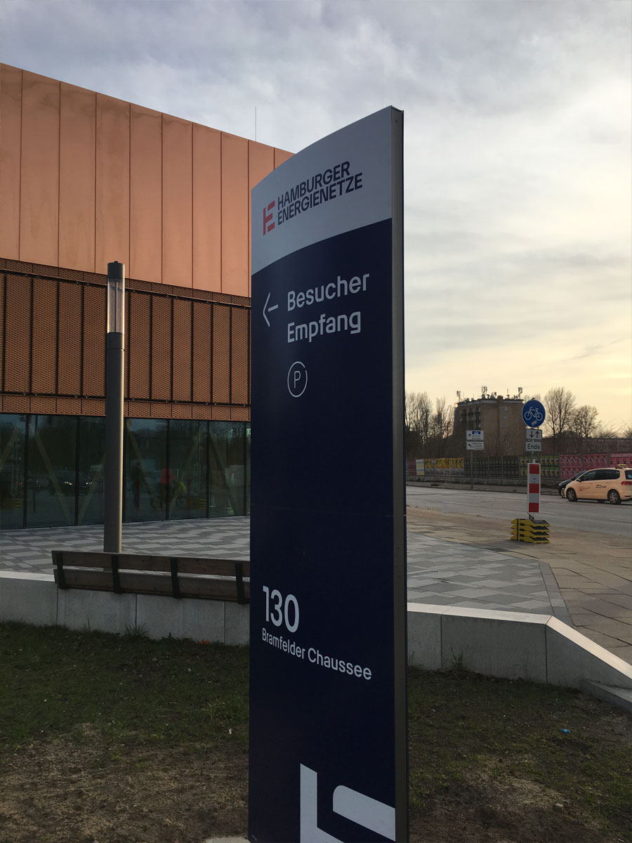Dunkelblauer Pylon von Hamburger Energienetze mit Wegweiser zu Besucherempfang und Parkplatz sowie der Hausnummer 130, Bramfelder Chaussee