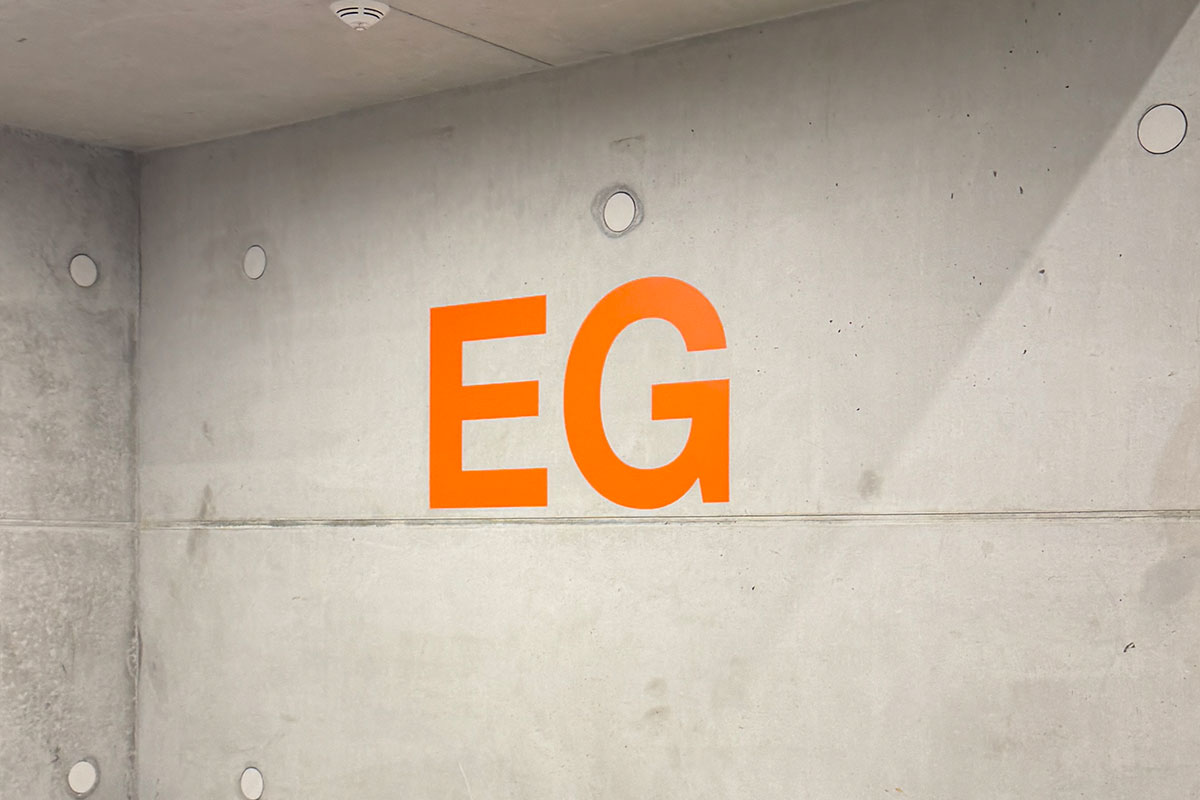 Orangefarbene Etagenkennzeichnung EG direkt auf einer Sichtbetonwand