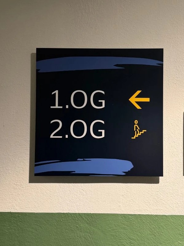 Quadratischer dunkelblauer Wegweiser: 1.OG mit gelbem Pfeil nach links, 2.OG mit gelbem Treppen-Piktogramm