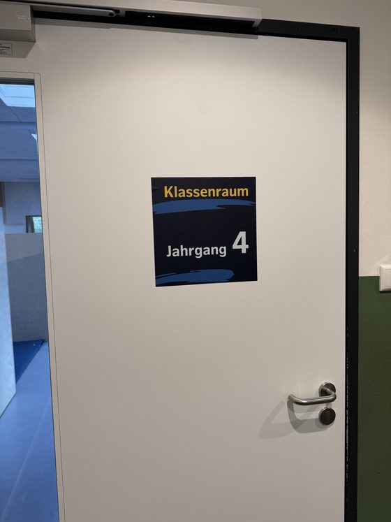 Schild als Folie auf einer weißen Tür: gelbe Aufschrift Klassenraum, darunter groß Jahrgang 4