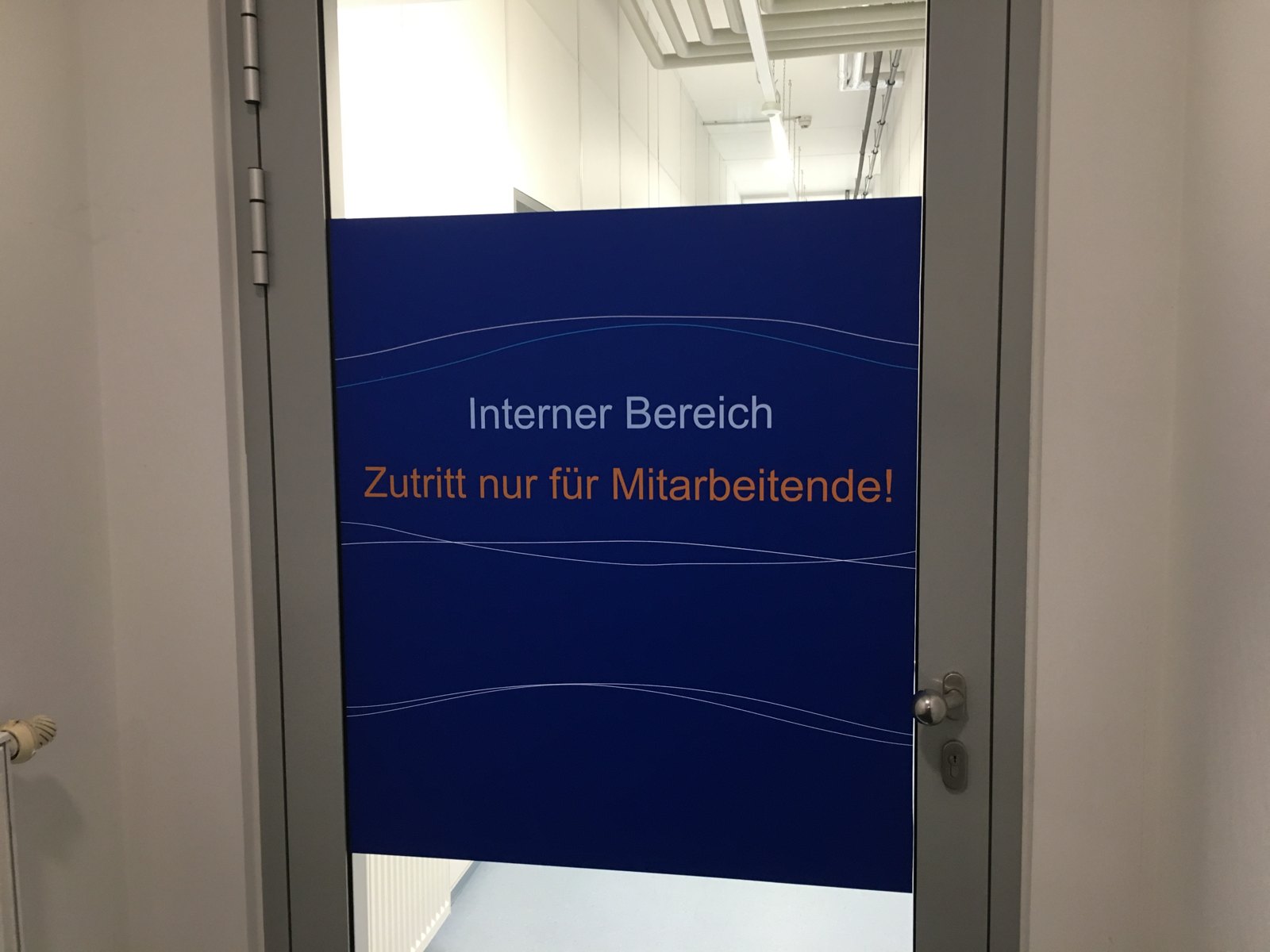 Glastür mit blauer Sichtschutzfolie und dem Hinweis Interner Bereich, Zutritt nur für Mitarbeitende
