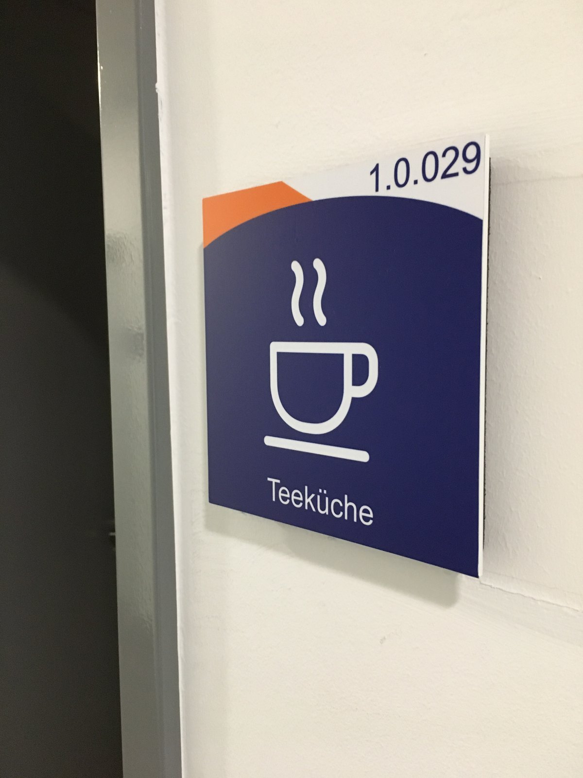 Türschild 1.0.029 mit Tassen-Piktogramm und der Bezeichnung Teeküche neben einer Türzarge