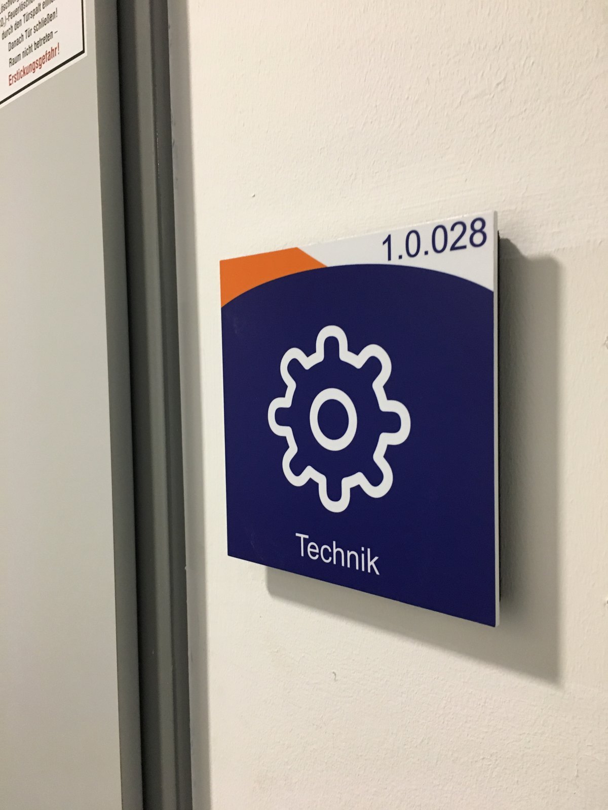 Türschild 1.0.028 mit Zahnrad-Piktogramm und der Bezeichnung Technik neben einer Türzarge