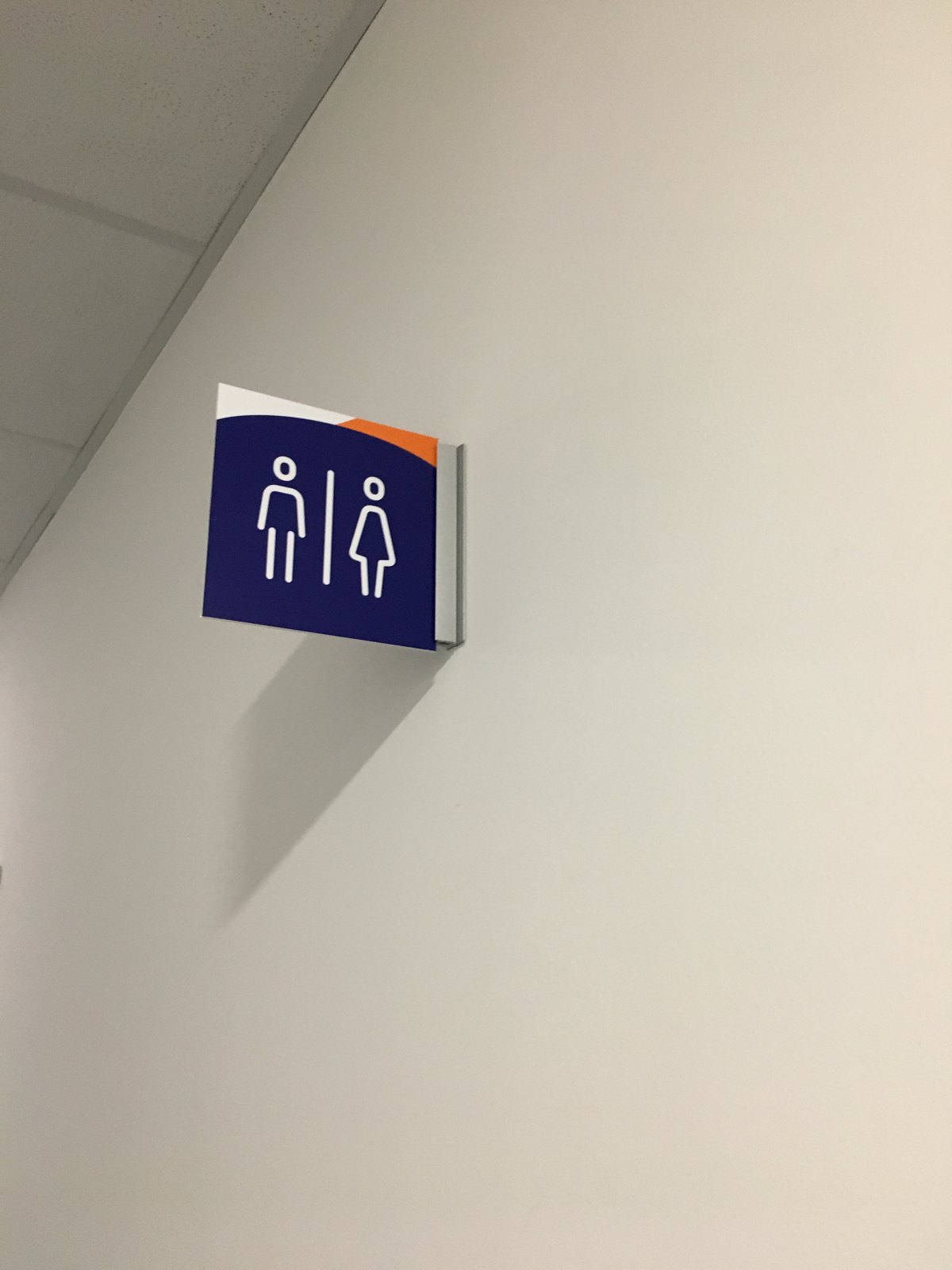 Flügelschild mit Piktogramm für WC Damen und Herren steht von einer weißen Wand ab