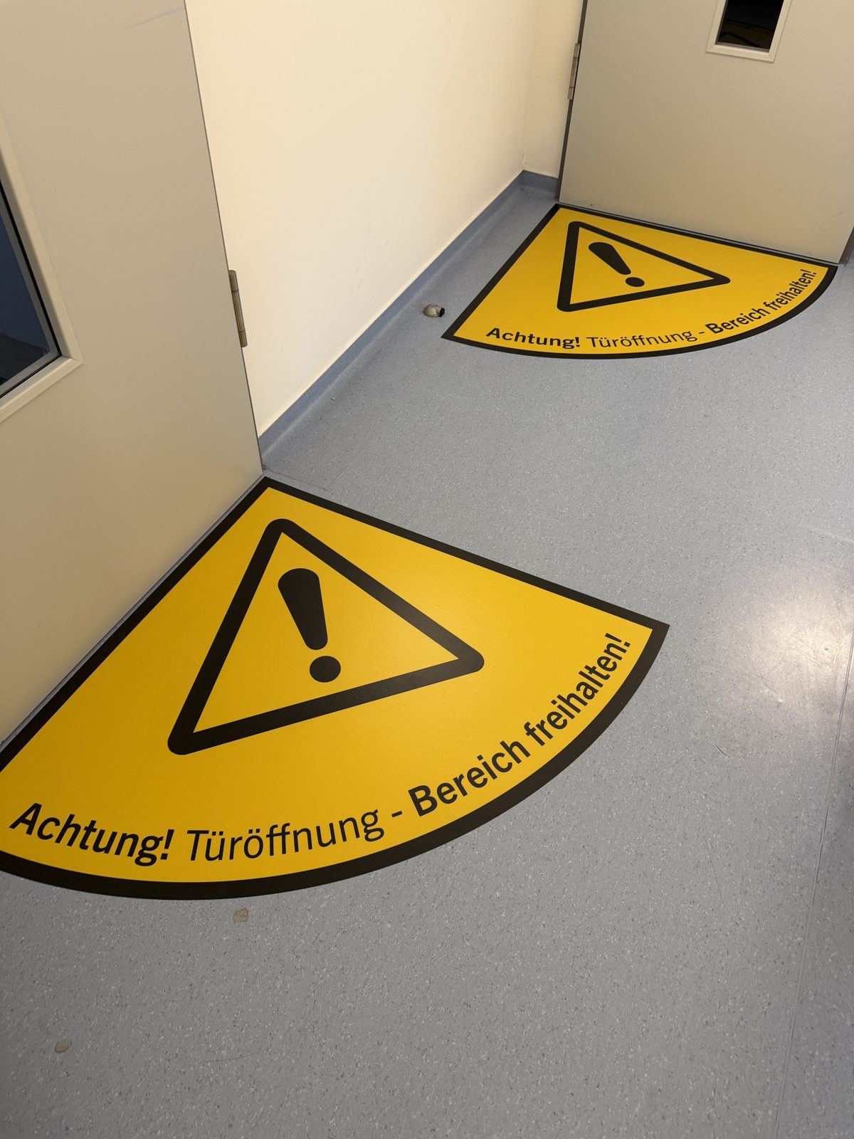 Gelbe Bodenmarkierung mit Warndreieck und dem Text Achtung Türöffnung, Bereich freihalten