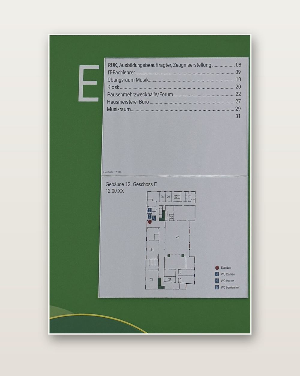 Geschosswegweiser E von Gebäude 12, freigestellt: oben die Raumliste mit Kiosk, Pausenmehrzweckhalle/Forum und Musikraum, unten der Plan des Erdgeschosses mit Legende, am unteren Rand ein Bogen mit gelber Linie