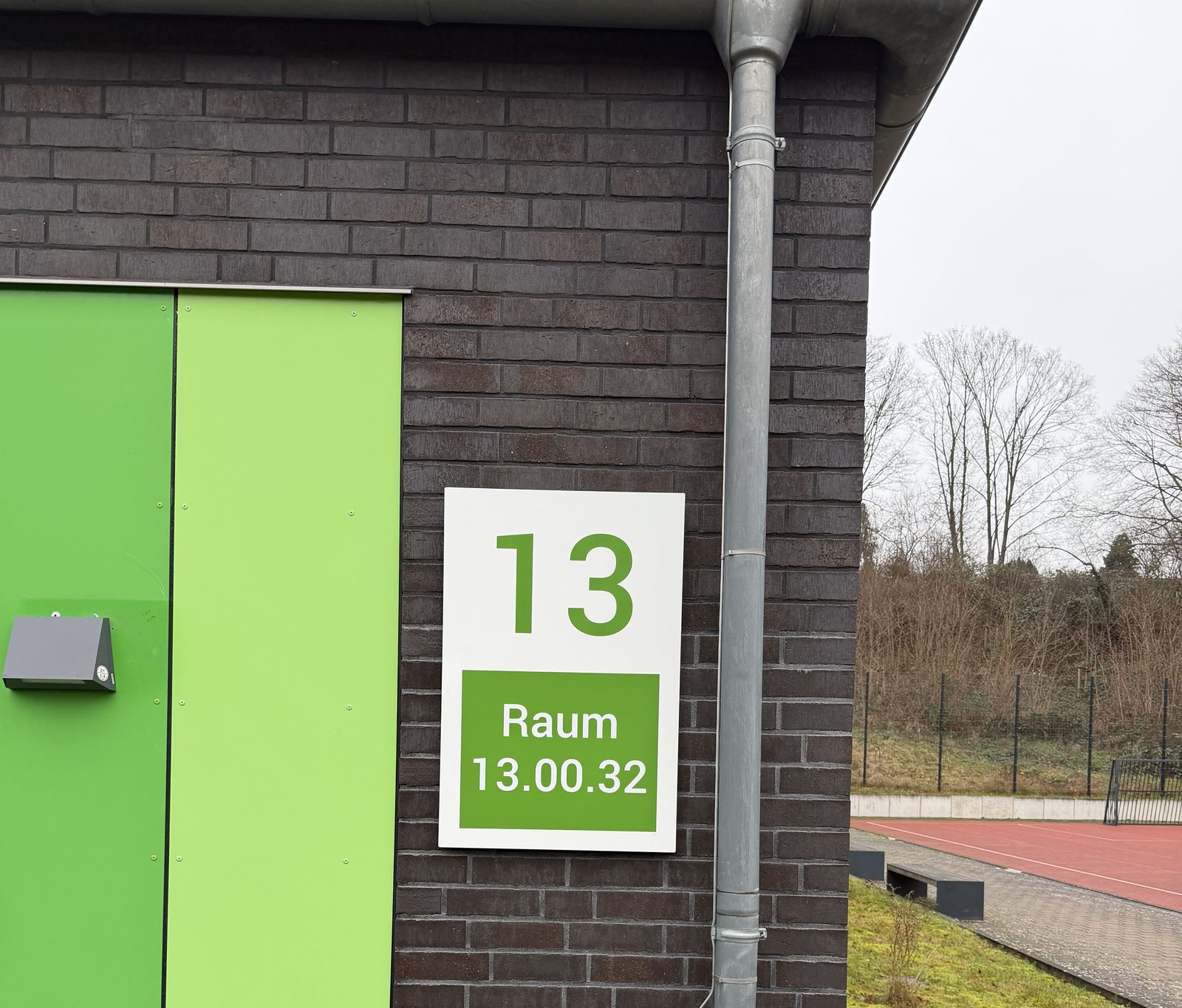 Grüne Fassadenplatten neben einem weißen Schild mit der Nummer 13 und dem Feld Raum 13.00.32