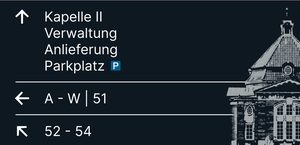 Wegweiser 2, Vorderseite: Pfeil ↑ Kapelle II, Verwaltung, Anlieferung, Parkplatz; Pfeil ← A–W, 51; Pfeil ↖ 52–54