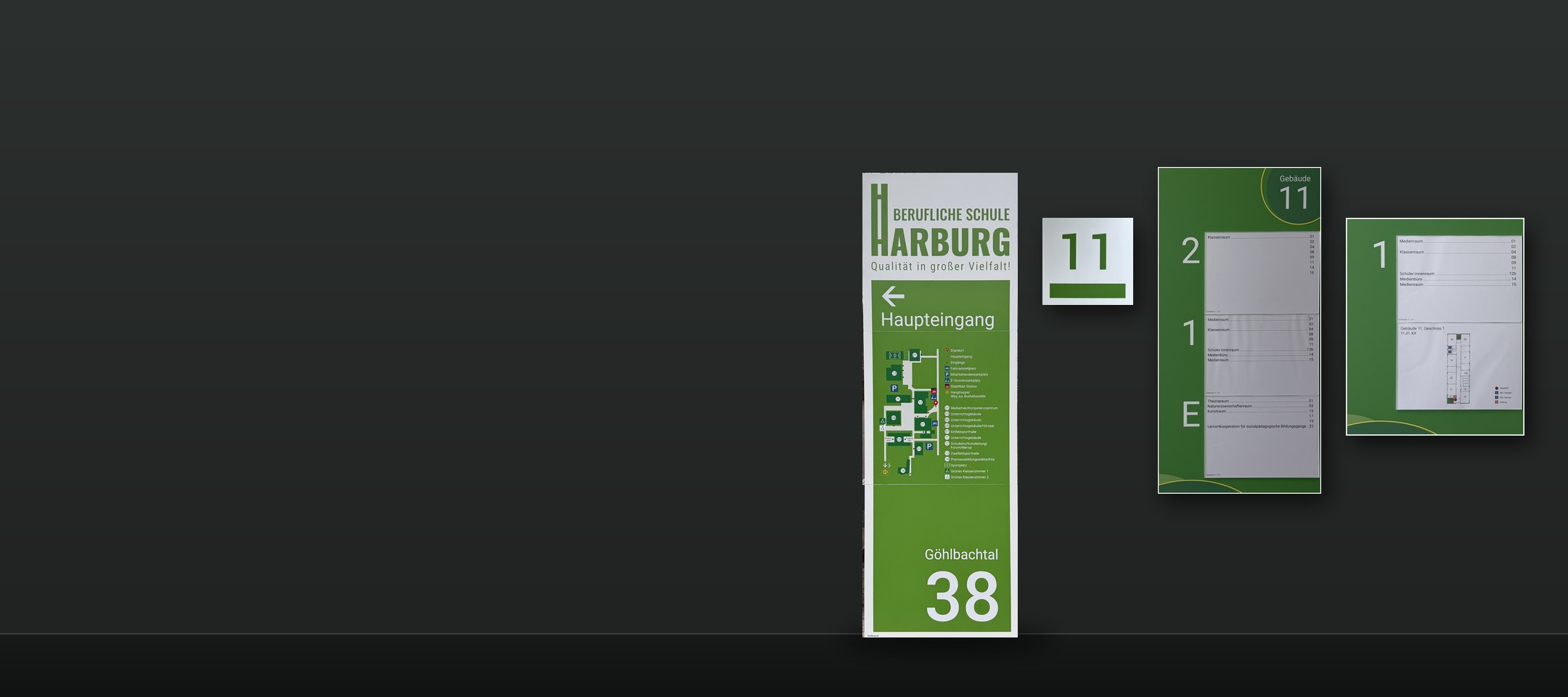 Die Elemente des Leitsystems freigestellt nebeneinander vor dunklem Grund: Monolith mit Lageplan, Gebäudenummer 11, Hauptwegweiser und Geschosswegweiser von Gebäude 11