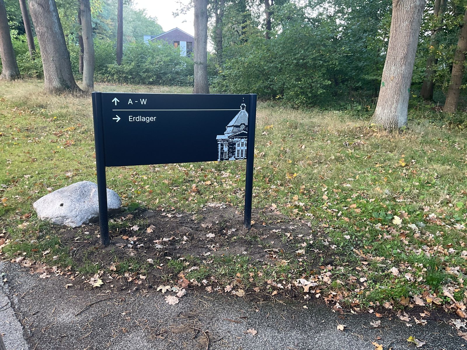 Wegweiser zwischen Bäumen mit Pfeil nach oben zu A bis W und Pfeil nach rechts zum Erdlager